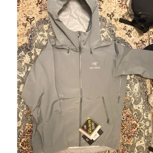 Arc'teryx beta SL vindjacka L - Snygg grå vindjacka från Arc'teryx i storlek L, tillverkad i slitstark Gore-Tex. Jackan har huva med dragsko, hel dragkedja framtill och två snedställda fickor med dragkedja. Perfekt för dig som vill ha en clean och funktionell look. Jag kan med all säkerhet lova att jackan inte tar in en enda droppe. Köpt fel storlek. Passar både m och L. Pris går altid att diskutera.