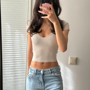 Beige ribbad croppad topp BikBok XS - Superfin croppad topp från BikBok i beige ribbat material. Toppen har korta ärmar, v-ringning med liten notch och sitter tight. Perfekt till jeans eller kjol för en chill och snygg look.