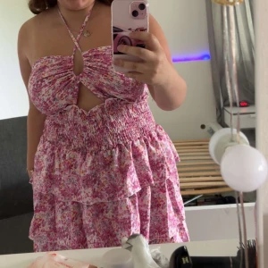 Blommig rosa långklänning med volanger - Testat en gång. Supersöt långklänning i rosa och vita toner med blommigt mönster. Klänningen har smockad midja, volanger och en snygg halterneck med cut-out framtill. 