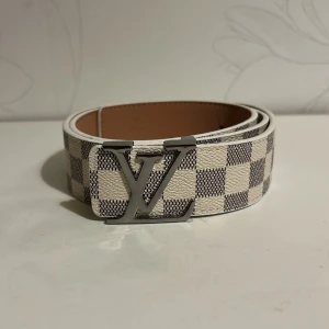 Bälte rutigt vit - Säljer ett snyggt bälte i vit med trendig rutig design längs bältet. Bältet är i storlek 110 men jag kan göra nya hål efter köp ifall det önskas. 