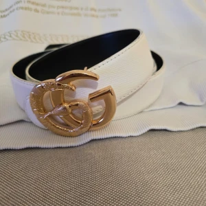 Vit skärp med guldspänne - Snyggt vitt skärp med ikoniskt GG-spänne i guld och ormdetalj. Bältet har en stilren design och är tillverkat i skinn med svart insida. Perfekt accessoar för att lyfta din outfit. Är dessutom ä.k.t.a
