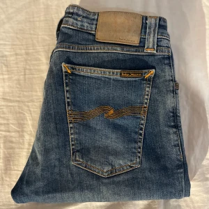 Blåa nudie jeans - Snygga blå jeans från Nudie Jeans med klassisk femficksdesign och kontrastsömmar. Jeansen har en rak passform och är tillverkade i mjukt denimtyg med subtila slitningar. Perfekta för en avslappnad och stilren look.