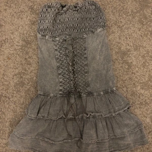 Grå volangklänning från Cotton Natural - Supersöt grå kortklänning från Cotton Natural med smockad rygg, snörning framtill och volanger i kjolen. Klänningen är ärmlös och har broderade detaljer upptill. Storlek xs/s men är väldigt töjbar så kan passa M också. Mycket bra skick och är endast använd 2-3 gånger. Matrialet är 100% bomull. Pris går att prutas