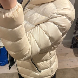Vit dunjacka från Colmar - Snygg dunjacka från Colmar med huva och dragkedja framtill. Jackan har quiltad design, två fickor med dragkedja och svart foder. Den har någon liten fläck men inget som är märkbart! Den är i storlek 45 (Italiens storlek) men är liten i storleken🤍 nypris 5 500kr