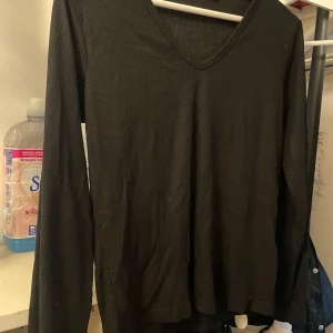 Svart ribbad långärmad tröja - Svart långärmad tröja med ribbad struktur och v-ringad hals. Enkel och stilren modell som funkar till många olika looks. Mjukt material som sitter skönt mot kroppen och har en normal passform.