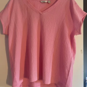 Rosa v-ringad topp från b.young - Säljer en rosa topp från b.young med v-ringning och korta ärmar. Toppen har en lätt strukturerad, krinklad yta och en loose passform som ger en chill vibe. Perfekt för dig som gillar färg och enkel stil.