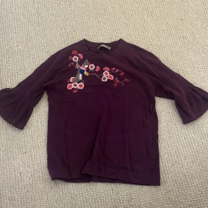 Broderad vinröd topp från Oasis - Supersnygg vinröd topp från Oasis med broderade blommor och fågel på bröstet. Toppen har trekvartsärmar med volang och en rak passform. Perfekt för dig som vill ha något unikt och färgstarkt i garderoben.