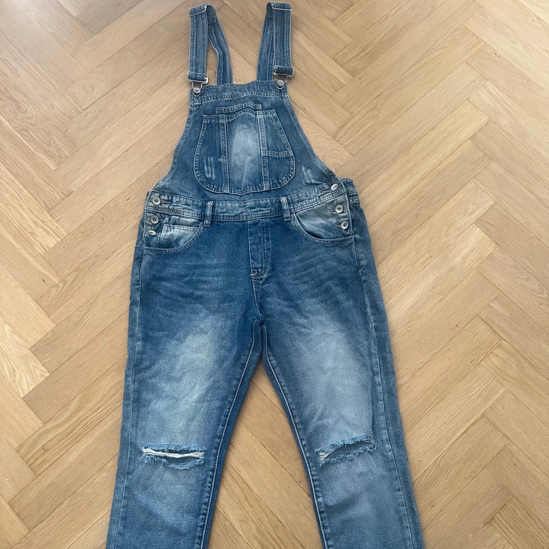 Blå denim hängselbyxor med slitningar