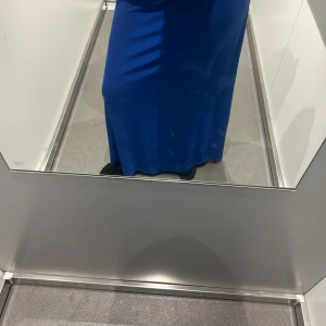 Blå lång tjol  - En stilren långtjol  i kornblå färg med rak passform. Tjolen har en enkel och elegant design utan synliga detaljer eller mönster, vilket ger ett modernt och minimalistiskt intryck. Perfekt för dig som gillar en klassisk look med färg.