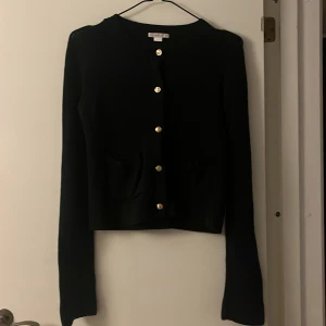 Svart kofta från Gina Tricot med guldknappar - Svart stickad kofta från Gina Tricot med snygga guldknappar framtill och två små fickor. Klassisk rund halsringning och långärmad modell, perfekt att slänga över en topp för en chill look.