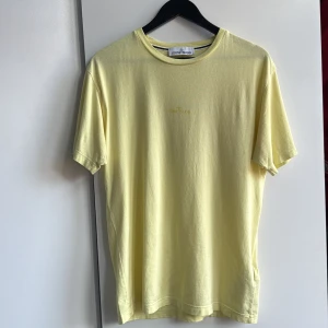 Gul t-shirt från Stone Island med reflextryck - Snygg gul t-shirt från Stone Island med tryckt logga på bröstet och ett stort reflekterande print på ryggen. Modellen är klassisk med rund hals och korta ärmar, perfekt för dig som gillar streetwear och vill sticka ut med coola detaljer.