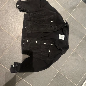 Svart jeansjacka från Pull&Bear - Svart jeansjacka från Pull&Bear med klassisk krage, silverfärgade knappar och två bröstfickor. Jackan har en rak, något croppad passform och är tillverkad i denim. Perfekt för dig som vill ha en stilren och tidlös look.❤️❤️❤️