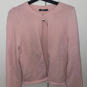 Ljusrosa kofta från Gina Tricot - Supersöt ljusrosa kofta från Gina Tricot med rund halsringning och knapp framtill. Koftan är stickad, har långa ärmar och en enkel, clean look som passar perfekt till lager-på-lager. Perfekt för dig som gillar en mjuk och feminin stil.