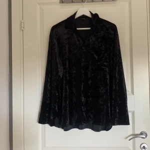 Svart sammetsskjorta Gina Tricot XS - Svart skjorta i mjuk sammet från Gina Tricot, storlek XS. Skjortan har klassisk krage, knappar framtill och en bröstficka. Långärmad och loose fit för chill vibe. Perfekt att styla med jeans eller kjol för en cool look.