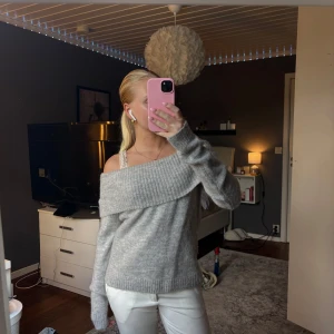 Grå offshoulder stickad tröja - Supermysig grå stickad tröja med bred offshoulder-krage och långa ärmar. Tröjan har en relaxed fit och ribbade muddar vid ärmslut och nederkant. Perfekt för lager-på-lager och chill vibes.