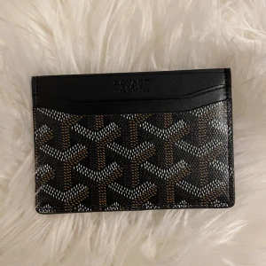 Goy4rd plånbok med ikoniskt mönster - Snygg och stilren plånbok från Goy4rd i svart med klassiskt grafiskt mönster i vitt och brunt. Tillverkad i exklusivt skinn och levereras med originalask, dustbag och kvitto. Perfekt för kort och sedlar, smidig att ha i fickan.