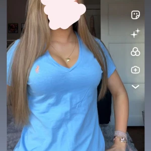 Blå v-ringad t-shirt från Ralph Lauren - Snygg ljusblå t-shirt från Ralph Lauren med klassisk v-ringning och korta ärmar. T-shirten har den ikoniska orangea Polo-loggan broderad på bröstet och är gjord i mjuk bomull som känns skön mot huden. Perfekt till jeans eller shorts för en chill look. aldrig använd!! 