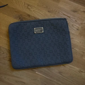 Mörk grå datorväska Marc by Marc Jacobs - Säljer en snygg datorväska från Marc Jacobs med präglade bokstäver över hela ytan och en metallbricka framtill. Väskan har dragkedja och är fodrad med mjukt material på insidan. Jättefint skick 