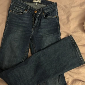 Mörkblå jeans från ONLY bootcut - Snygga mörkblå jeans från ONLY med klassisk femficksdesign och bootcut-ben. Jeansen har gylf med dragkedja och knapp upptill. Midwaist.