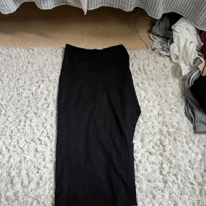 Svart långkjol i bomull med slits  - En stilren svart långkjol med rak passform. Kjolen är enkel och tidlös, perfekt för dig som gillar minimalistisk stil. Tillverkad i mjukt bomullstyg som känns skönt mot huden. Passar till många olika looks och är lätt att matcha med andra plagg.