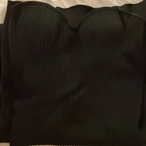 Svart ribbad klänning - Snygg svart klänning med ribbad struktur och hjärtformad urringning. Har en slits.