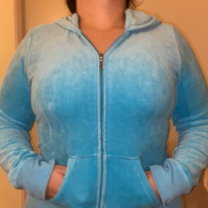 Blå velour hoodie från Juicy Couture - Säljer en ikonisk ljusblå hoodie från Juicy Couture i mjuk velour. Tröjan har dragkedja, huva och fickor framtill. Baksidan är dekorerad med glittriga stenar som bildar Juicy Couture-loggan och en krona. Perfekt för en chill och trendig look. De är storlek xxxl men de är som m och s för de är små i storlek. Säljer i complet med byxor 