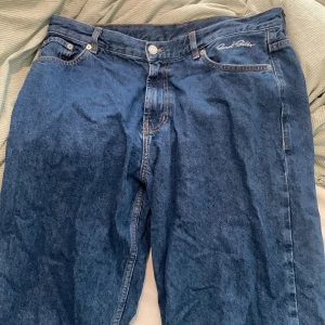 Blå jeans från Sweet SKTBS, medium - Blå jeans från Sweet SKTBS med klassisk femficksdesign och broderad logga vid fickan. Jeansen har en rak passform och är tillverkade i robust denim. Snygga slitningar och ljusare partier vid bensluten ger en cool, avslappnad vibe.