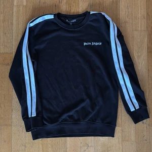  Palm Angels sweatshirt  - Svart sweatshirt från Palm Angels med vita och ljusblå dubbla ränder längs ärmarna. Sällsynt tröja. Använd fåtal gånger men knappast tecken på användning. Passar både M och L. 