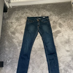 Replay mörkblå slim jeans - Snygga mörkblå jeans från Replay slim fit med låg midja och klassiska fem fickor. Jeansen har guldfärgade detaljer och kontrastsömmar som ger en cool look. Perfekta för dig som gillar en slim passform och stilren design.