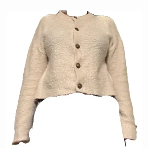 Beige kofta från Amisu (New yorker) med knappar - Supermjuk och mysig beige kofta från Amisu med stora dekorativa knappar framtill. Koftan är croppad, har lång ärm och ribbade detaljer vid hals, ärmslut och nederkant. Perfekt för lager-på-lager och chill dagar.