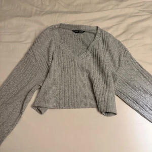 Grå croppad stickad tröja Shein - Säljer en grå croppad stickad tröja från Shein med v-ringad hals och ribbad struktur. Tröjan har långa ärmar och en loose passform som ger en chill vibe. Perfekt för dig som gillar enkla och snygga plagg med lite edge.