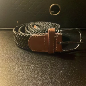 Grisch svart flätat bälte - Snyggt svart flätat bälte med bruna skinn-detaljer och silverfärgat spänne. Bältet har en stilren och tidlös look med tydliga sömmar på skinnet. Perfekt accessoar för att lyfta din outfit med en klassisk touch. Går att diskutera priset😁