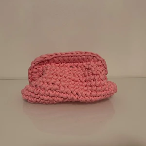 Handgjord rosa kuvertväska i bomull - Unik handgjord kuvertväska i ljusrosa, virkad i tjockt T-shirt garn. Väskan har en mjuk, boxig form och öppnas upptill. Perfekt för dig som vill sticka ut med en färgglad accessoar.