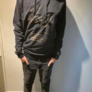 Mörkgrå hoodie från Jack & Jones - Säljer en mörkgrå hoodie från Jack & Jones med stor J&J-logga och text framtill i beige. Tröjan har huva med snören och långa ärmar. Perfekt för dig som gillar en enkel och stilren look. Hör av er vid funderingar, jag själv på bilden är 165-170