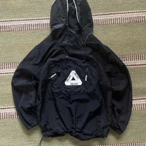 Svart vindjacka från Palace - Svart vindjacka från Palace, storlek S. Jackan har huva med snörning och justerbar nederkant. Bra skick, 7-8/10
