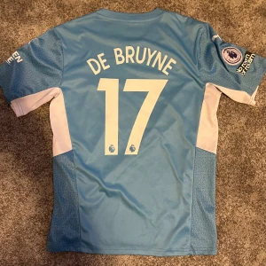 Manchester City De Bruyne tröja Puma - Säljer en Manchester City matchtröja med De Bruyne 17 på ryggen. Tröjan är ljusblå med vita detaljer, kortärmad och har tryckta loggor från Puma, Etihad Airways och Premier League. PERFEKT FÖR RIKTIGA FOTBOLLSFANS