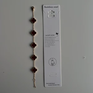 Red/Wine-gold Alhambra’s bracelet  - Snyggt armband i guldtonad metall med fem röda klöverformade hängen. Kedjan är tunn och elegant, och varje klöver har en pärlad kant som ger extra detalj. Perfekt för dig som vill ha något unikt och stilrent på handleden. Mvh clover.se