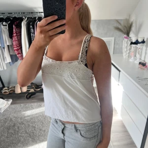 Vit linnetopp med spetsdetaljer - Säljer en söt vit linnetopp med broderade spetsdetaljer upptill och smala axelband. Toppen är croppad och har en luftig passform, perfekt för varma dagar. Materialet känns mjukt och bekvämt mot huden.