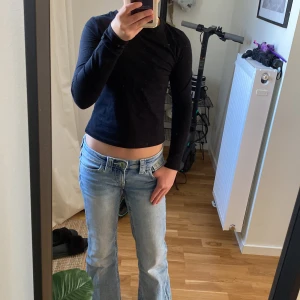 Svart långärmad topp från H&M - En svart, enkel långärmad topp från H&M i mjuk bomull. Modellen är croppad och har en tight passform som sitter snyggt på kroppen. Perfekt att matcha med jeans eller kjol för en clean look.