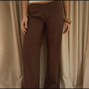 Bruna wide lågmidjade byxor med struktur - Säljer ett par bruna byxor från Nelly med snyggt strukturerat tyg och breda ben. De har en enkel midja och ett stilrent, avslappnat snitt som ger en cool vibe. Perfekta för dig som gillar trendiga och bekväma byxor med lite extra känsla i materialet.