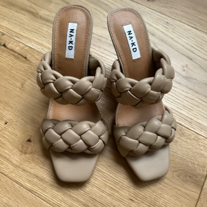 Beige flätade sandaler från NA-KD - Snygga beige sandaler från NA-KD med två breda flätade remmar och fyrkantig tå. Skorna har låg klack och är tillverkade i mjuk syntet (polyuretan) med gummisula. Perfekt för dig som gillar trendiga detaljer och stilren design.