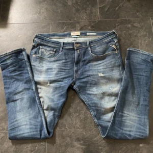 Repley anbass jeans - Säljer ett par blå Replay jeans med snygga slitningar och ljusa tvättade partier. Klassisk femficksmodell med dragkedja och läderpatch bak. Jeansen är i ett gott skick. Inga defekter på dom. Perfekt nu till hösten 🤩🍂 kom med frågor och funderingar🤗 priset är inte fast i sten!!