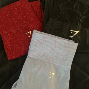 Gymshark seamless leggings i tre färger - Säljer tre par Gymshark seamless leggings i rött, svart och blå/lila. Alla har hög midja och något typ av  mönster, med Gymshark-logga framtill. Dessa tre är helt nya och alltså aldrig använda, säljer de därför då de ej kommer till användning. Ordinarie:599/styck. Man kan köpa alla tre för 1200kr , 2 för 850 eller 1 för 450