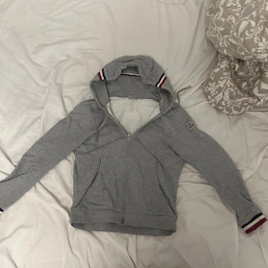 Moncler Hoodie/zip Grå strl L/3 - Snygg och exklusiv hoodie från Moncler i klassisk grå färg. Tillverkad i mjukt och lyxigt bomullsmaterial med perfekt passform. Dragkedja framtill, två fickor och diskret Moncler-logga på ärmen.