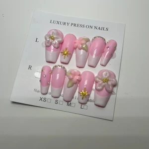 Lyxiga rosa press-on naglar med blommor - Säljer ett set med lyxiga press-on naglar i ljusrosa och vitt med 3D-blommor, pärlor och guldstjärnor. Naglarna har en elegant, lång form och dekoreras med detaljer i guld och pastell. Perfekt för dig som vill ha en söt och unik nageldesign. Obs handgjorda utav mig själv  därav pris 