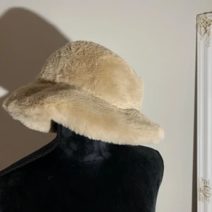 Beige fuskpäls bucket hat - Supermjuk och fluffig bucket hat i beige fuskpäls från ASOS DESIGN. Aldrig använd. Omkrets ca 55cm. Pris: 10kr 