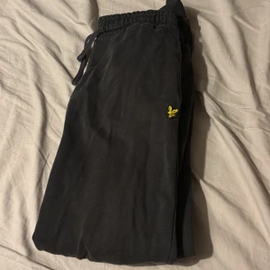Svarta mjukisbyxor Lyle & Scott Junior - Svarta mjukisbyxor från Lyle & Scott Junior med resår och snörning i midjan. Byxorna har en gul broderad logga på benet och en bakficka. Perfekta för chill eller träning, riktigt sköna och stilrena.