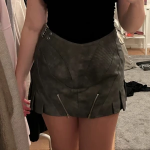 Grå kjol med dragkedjor från EGO - Säljer en grå kortkjol från EGO med coola detaljer som två dragkedjor framtill. Kjolen har en edgy vibe och passar perfekt till en trendig outfit.