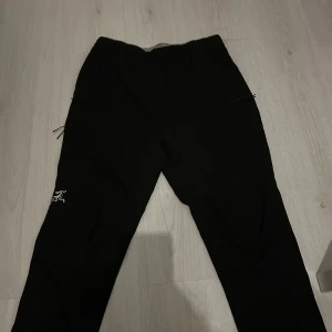 Svarta Arc'teryx byxor  - Svarta byxor från Arc'teryx med elastisk midja och snörning. Byxorna har smal passform, dragkedjeförsedda fickor och diskret Arc'teryx-logga på benet. Perfekta för dig som gillar stilrena och funktionella plagg. Passformen är typ XS eller S. Jag har haft dom i ca 1 år då jag säljer dom för dom är för små. Dom är också lite slitna vid foten av byxorna. Samt har också en airflow på sidan. 