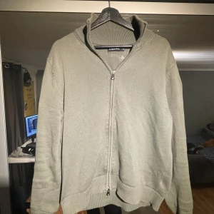 Olivgrön stickad kofta från J.Lindeberg - Säljer en olivgrön stickad kofta från J.Lindeberg i storlek M. Koftan har hel dragkedja framtill, ribbad krage och muddar samt långärmad passform. Perfekt för lager-på-lager och chill stil.